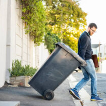 Man pulling a wheeled dumpster out of his garage while going to work Man pulling a wheeled dumpster out of his garage while going to work